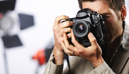 Young man taking photo with professional digital camera focus on hand and lens